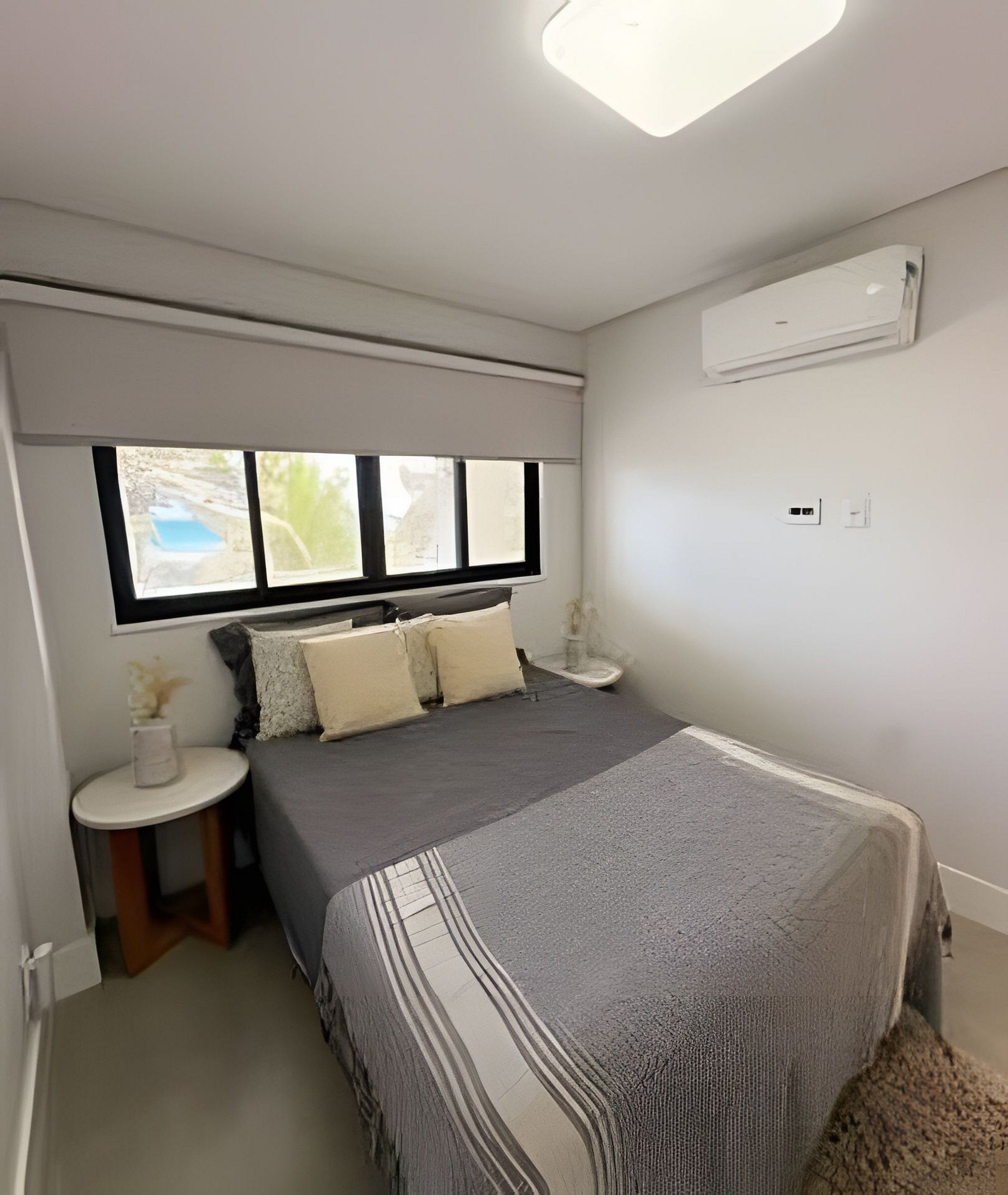 Un dormitorio con cama, mesita de noche, ventana y equipo de aire acondicionado.