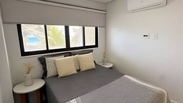 Un dormitorio con cama, mesita de noche, ventana y equipo de aire acondicionado.
