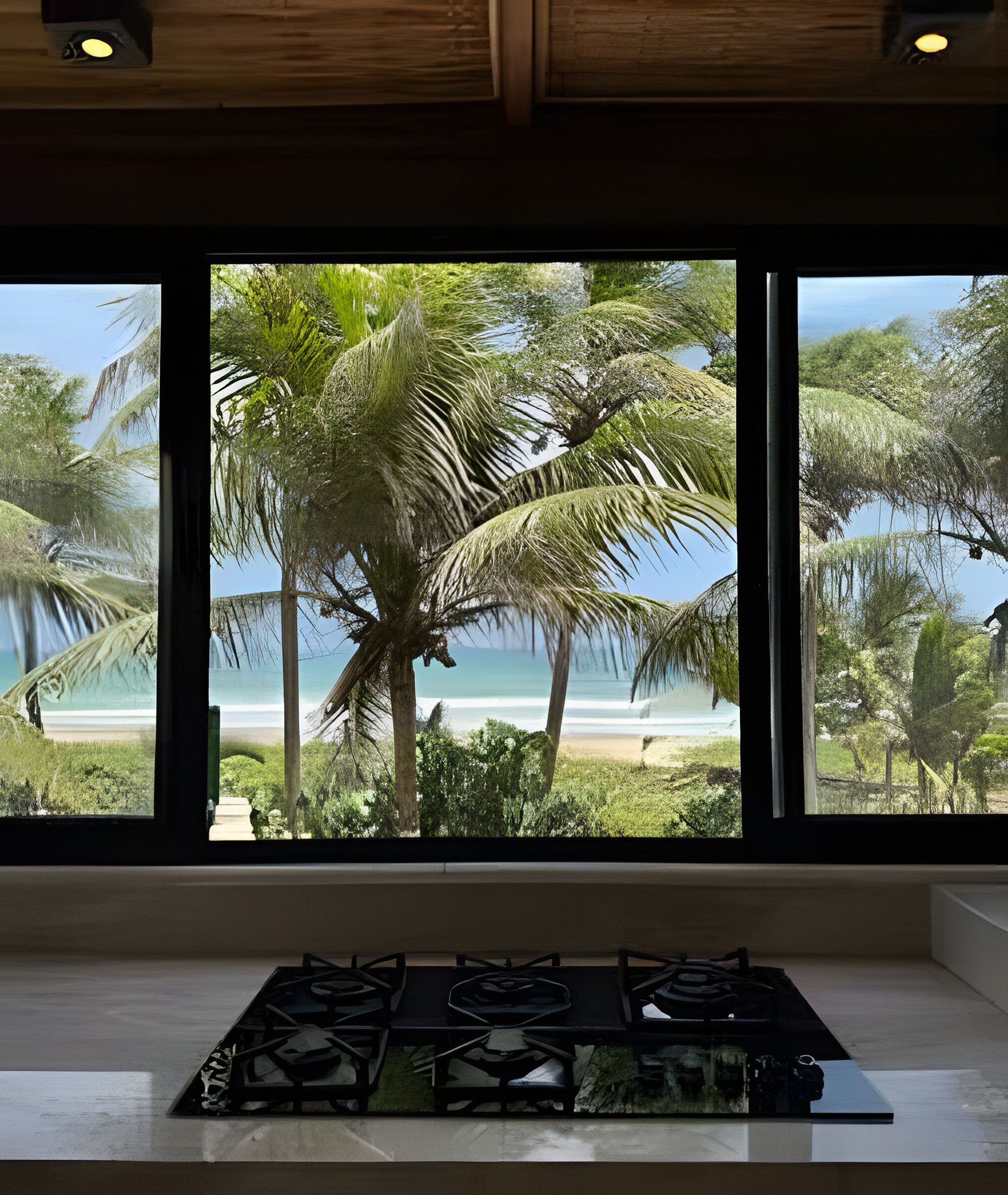 Una cocina con estufa a gas y vista a una playa con palmeras.