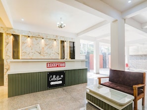 A reception area with a marble wall, a reception desk, a couch, and a glass coffee table. - Saver Double bhu iit Mahamanpuri (Varanasi)