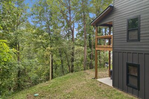 A house with a covered porch, surrounded by a wooded area. - Modern Mountain Chalet | Views, Hot Tub & Fire Pit (Gatlinburg)