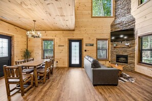 A wooden interior with a dining area, a sofa, a fireplace, and a stone accent wall. - Modern Mountain Chalet | Views, Hot Tub & Fire Pit (Gatlinburg)