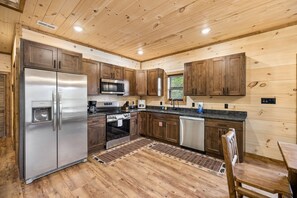 A modern kitchen with wooden cabinets, stainless steel appliances, and a black countertop. - Modern Mountain Chalet | Views, Hot Tub & Fire Pit (Gatlinburg)