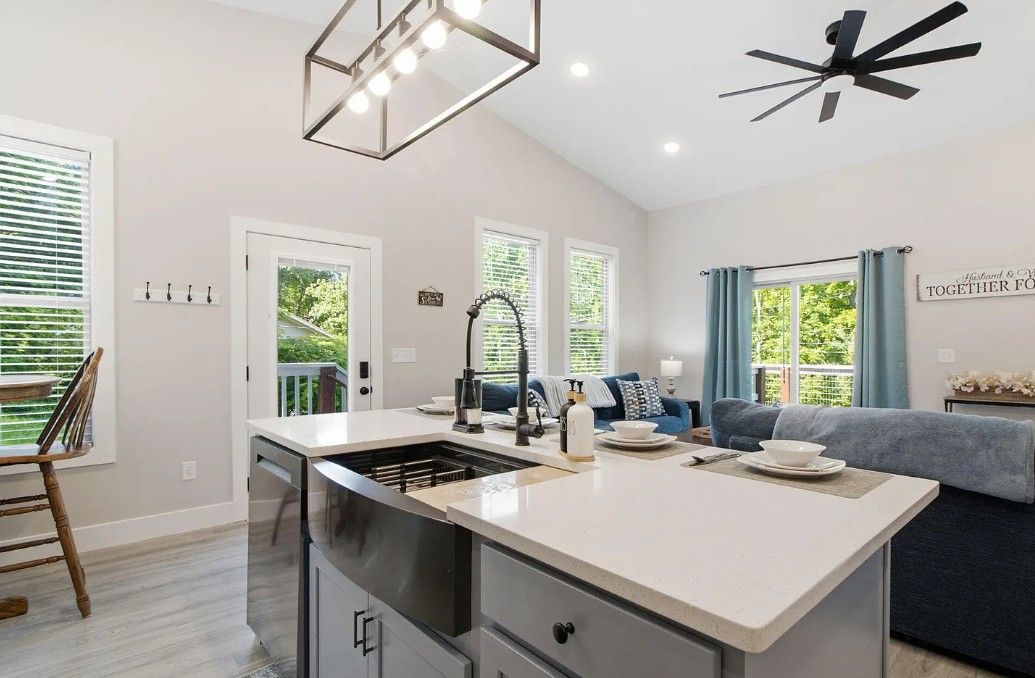 A modern kitchen with a central island, a dining area, and a living space with a sofa and a ceiling fan.