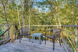 Een houten terras met twee rieten stoelen en een kleine tafel, omringd door een metalen hekwerk en weelderige beplanting.