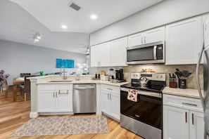 A modern kitchen with white cabinets, stainless steel appliances, and a marble countertop. - 4505 Minutes to Magic! 3/3 Resort Condo Near Disney (Orlando)