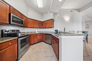A modern kitchen with wooden cabinets, stainless steel appliances, and a granite countertop. - 4507 Spacious 3/2 Resort Condo Near Disney (Orlando)