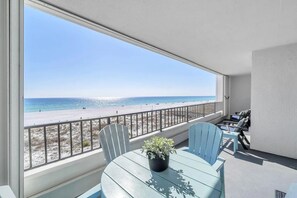 Un balcón con vista a la playa, una mesa con sillas y una planta en maceta.