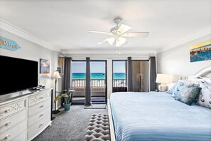 Una habitación de hotel con una cama, televisión, ventilador de techo y vista a la playa.