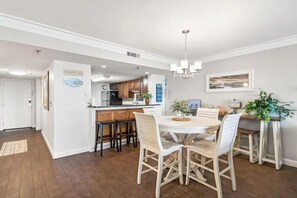 Una cocina moderna con armarios de madera, un comedor con mesa y sillas blancas, y un pasillo con alfombra.