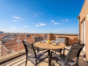 A rooftop terrace with a round table and chairs, a bowl of fruit, and a view of the cityscape. - Amielie with lateral seaview by Interhome (Blankenberge)