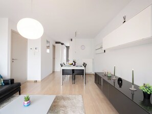 Ein modernes Wohnzimmer mit Essbereich, einer schwarzen Couch, einem Couchtisch mit Pflanze und einer großen, runden Leuchte.