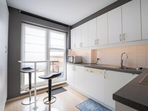 Une cuisine moderne avec des meubles blancs, un évier en acier inoxydable et une fenêtre équipée de stores.