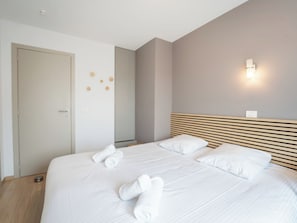 Une chambre d’hôtel avec un grand lit, une tête de lit en bois, un luminaire fixé au mur et une porte dotée d’une poignée.