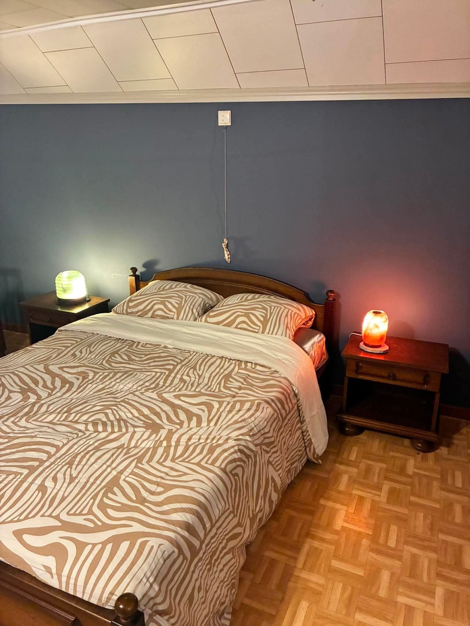 Un dormitorio con cama, dos mesitas de noche, cabecera de madera y una lámpara en el techo.