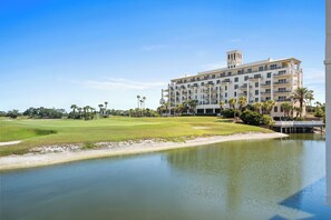 Een meerlaags hotel met een zwembad, een golfbaan en palmbomen.