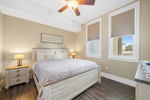 Ein Schlafzimmer mit einem Bett, Nachttischen, einem Deckenventilator und einem Fenster mit Jalousien.