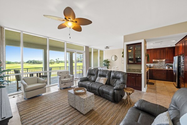 Ein geräumiges Wohnzimmer mit einer Ledersofa, einem Couchtisch und Blick auf einen Golfplatz durch große Fenster.