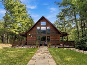 A wooden cabin with a porch, stone pathway, and a view of the surrounding forest. - Luxury Home|Steps from Whiteface|Near Lake Placid (Wilmington)
