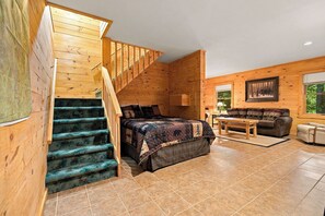 A wooden cabin interior with a staircase, a bed, a sofa, and a dining table. - Luxury Home|Steps from Whiteface|Near Lake Placid (Wilmington)