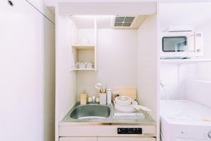 A compact kitchenette with a sink, microwave, and storage shelves. - Chic 1 Bedroom Space Near Nakasu (Fukuoka)