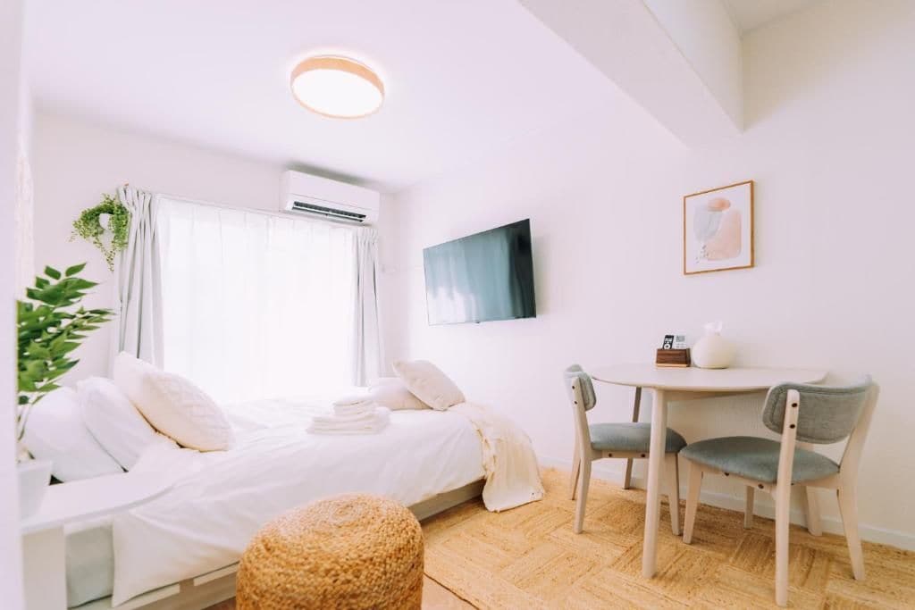 A room with a bed, a small table with chairs, a wall-mounted TV, and a window with curtains.