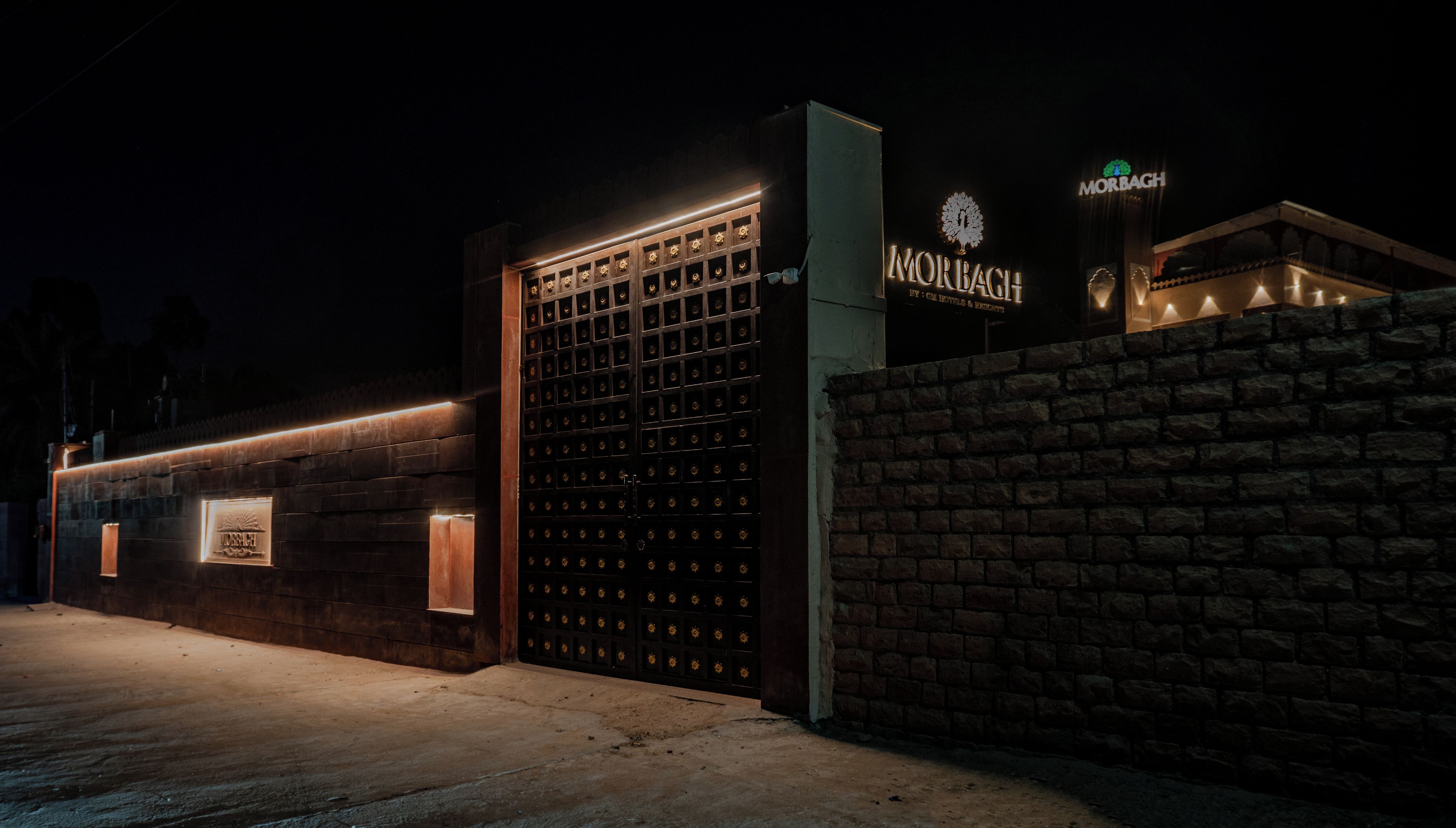 Entrada de hotel com um grande portão de metal, parede de tijolos e letreiros iluminados.