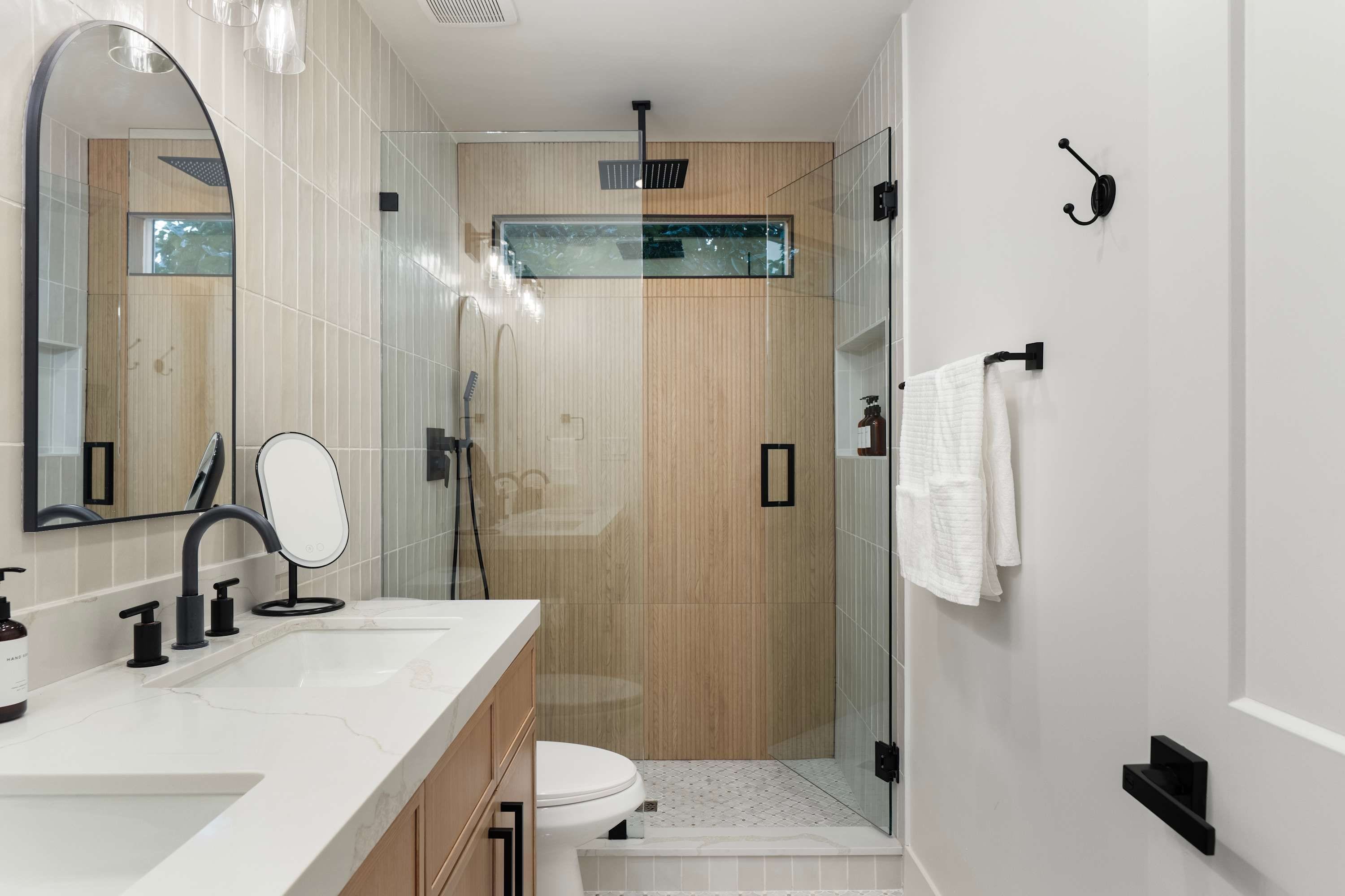 A modern bathroom with a large mirror, a shower, and a toilet.