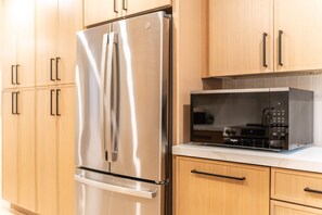 A stainless steel refrigerator with a freezer compartment, a microwave oven, and wooden cabinets with black handles. - The Belmont - Kierland (Scottsdale)