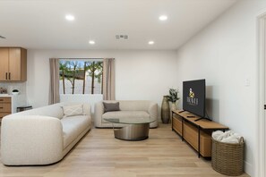 A modern living room with a sofa, a glass coffee table, a TV on a wooden stand, and a wicker basket. - The Belmont - Kierland (Scottsdale)