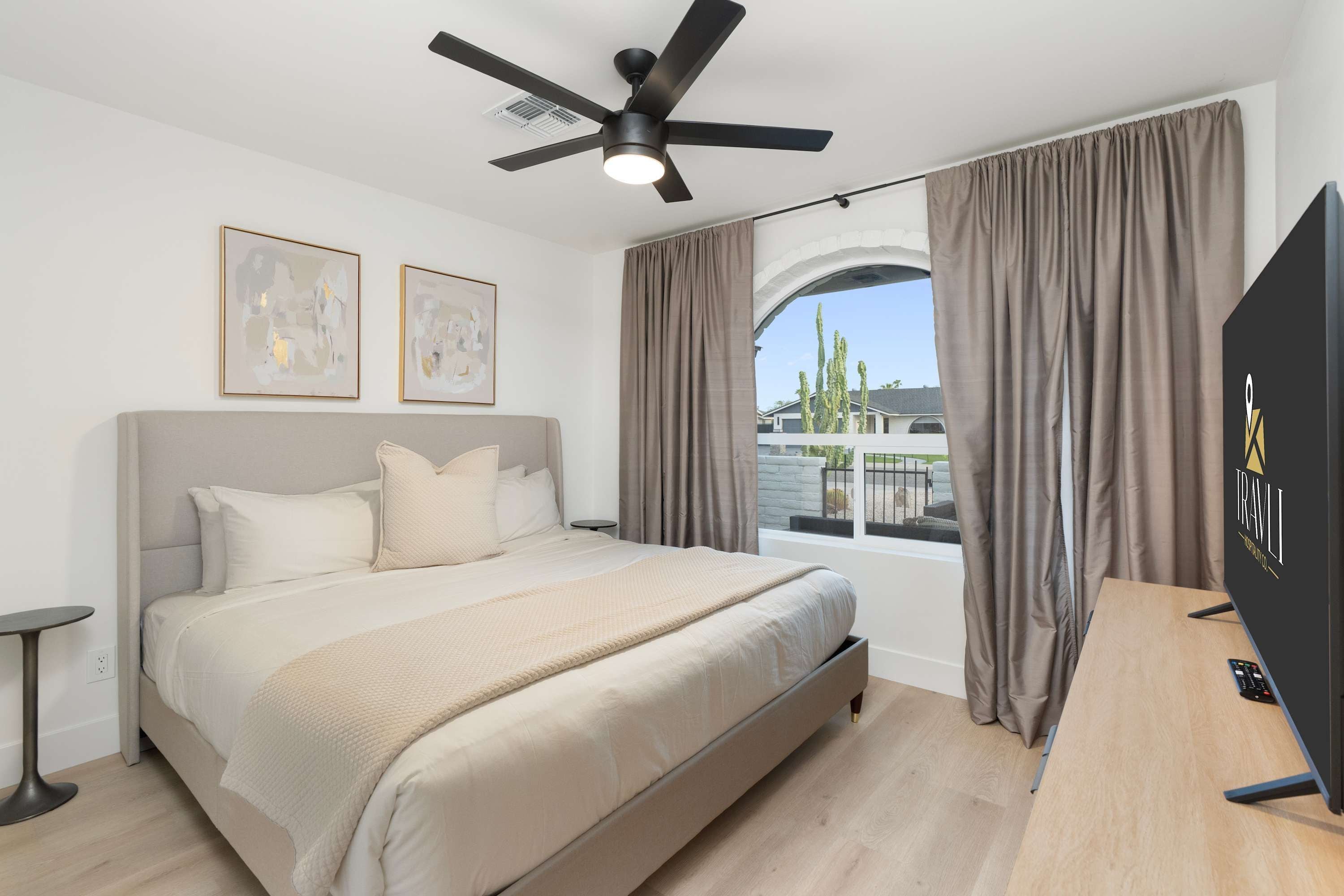 Une chambre moderne avec un grand lit, un ventilateur de plafond et un téléviseur posé sur un bureau en bois.
