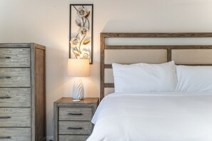 A bedroom with a wooden headboard, a bed with white bedding, a nightstand with a lamp, and a wooden dresser. - NEW Alta Mesa Retreat Pool Games More Sleeps 10 (Mesa)