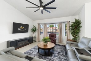 Un salon moderne avec une cheminée, un ventilateur de plafond, un canapé, une table basse et un téléviseur fixé au mur.