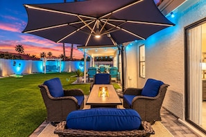 An outdoor patio with wicker furniture, a table with a fire feature, and a large umbrella. - NEW Alta Mesa Retreat Pool Games More Sleeps 10 (Mesa)