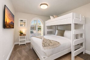 A bunk bed room with a large window, a bedside table with a lamp, and a framed picture on the wall. - NEW Sonoran Sol Modern Pool Oasis Near Kierland (Scottsdale)