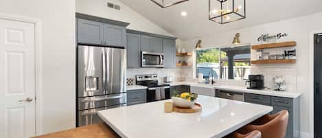 Una cocina moderna con una isla grande, electrodomésticos de acero inoxidable e iluminación colgante.