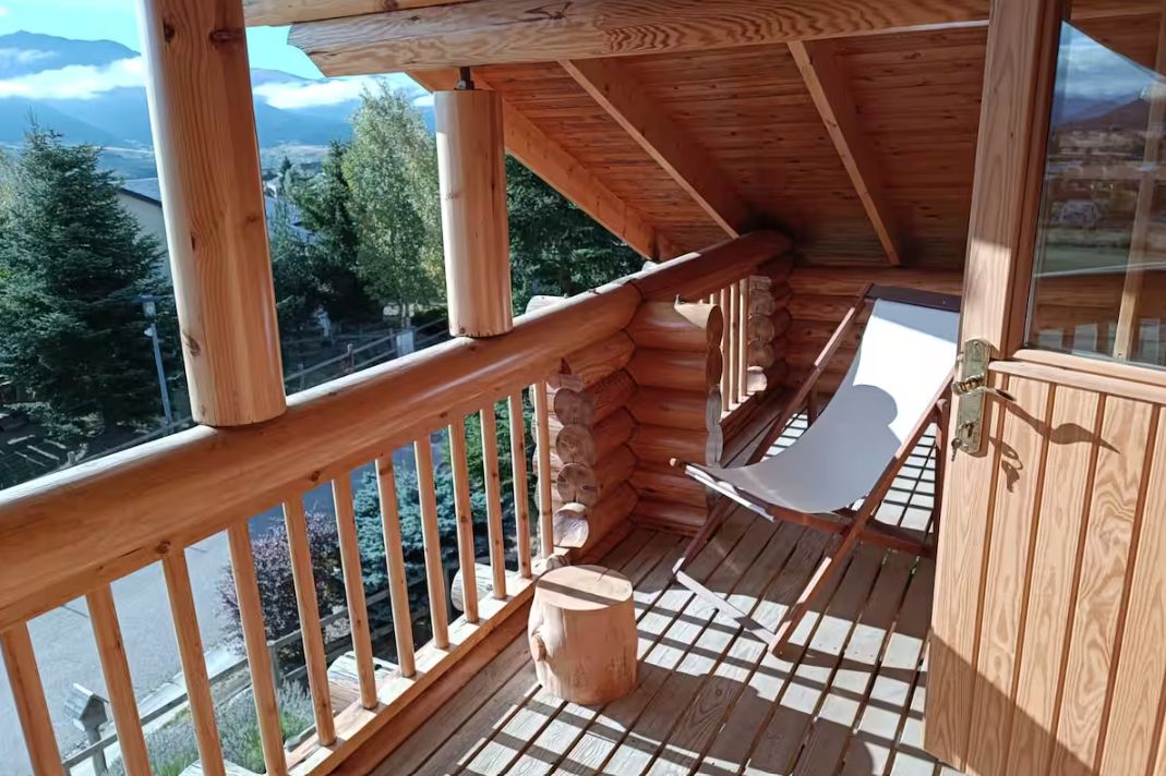 En træhytte med balkon, stol og bord.