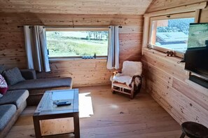 Ein gemütliches Blockhaus-Interieur mit einer Couch, einem Sessel, einem Couchtisch und einem Fenster mit Vorhängen.