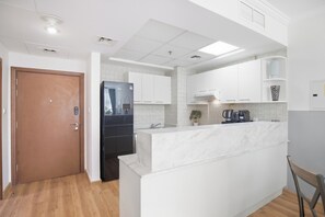 A modern kitchen with white cabinetry, a marble countertop, and a black refrigerator. - Luxury1BR in Downtown/Next Dubai Mall & Burj Khalifa (Dubai)
