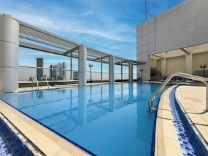 Una piscina interior con vistas despejadas de un horizonte urbano, un solárium con baldosas y una estructura de pérgola.