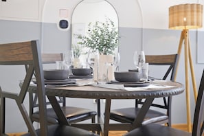 Una mesa de comedor dispuesta con platos, tazones, cubiertos y vasos, rodeada de sillas.