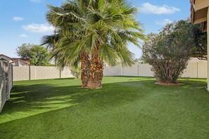 Ein Garten mit Kunstgrasanlage, einer Palme und einem kleinen Strauch.