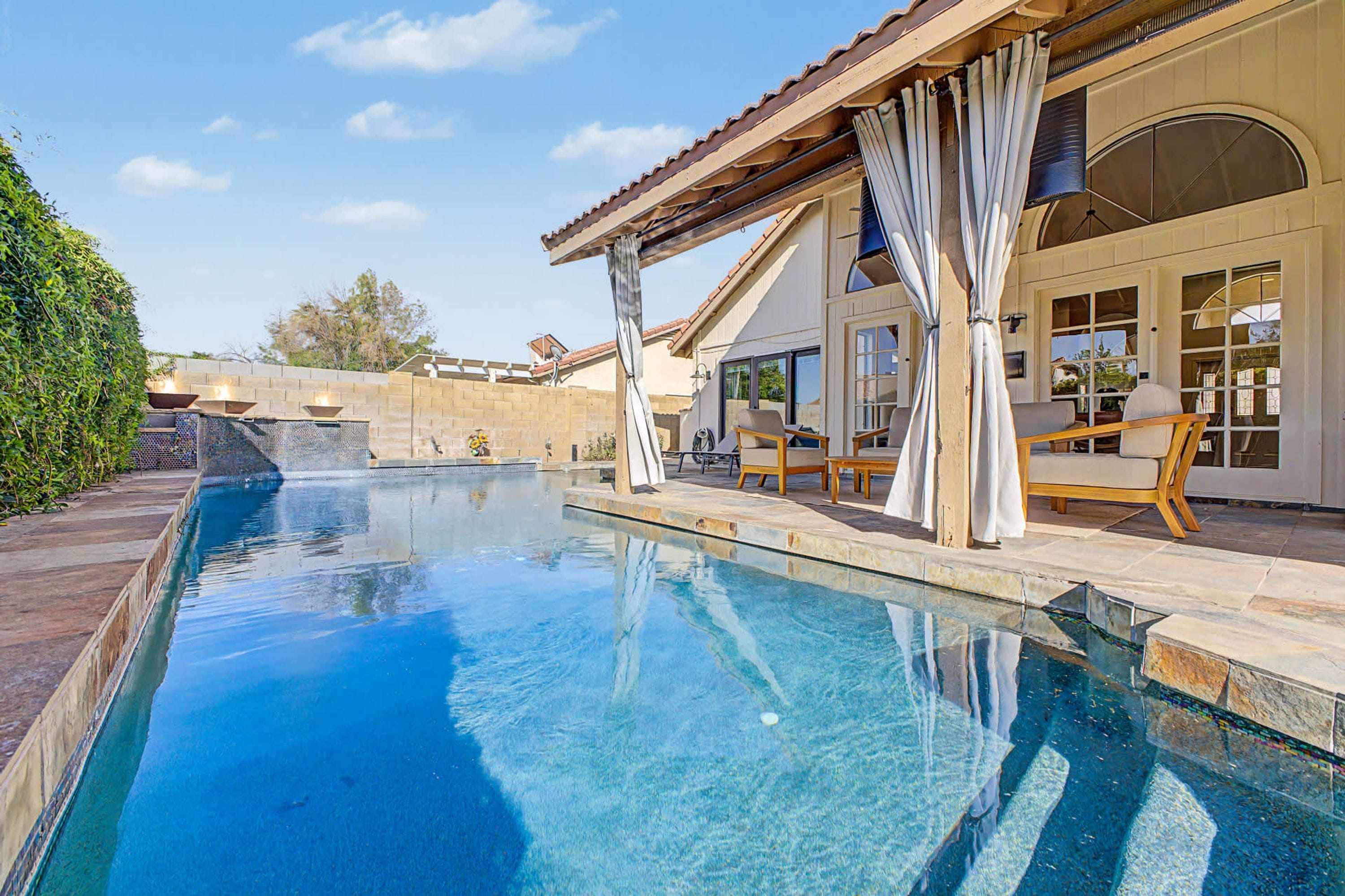 Una piscina con una pérgola y zona de estar al aire libre.