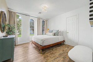 Ein Schlafzimmer mit einem hölzernen Bett, einem Nachttisch, einem Spiegel und einem Fenster mit Vorhängen.