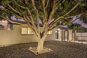 Une maison avec un grand arbre devant, un mur en briques et un petit jardin.
