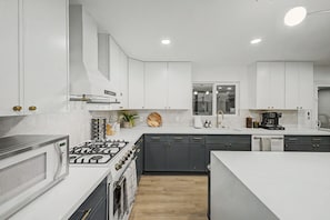 Une cuisine moderne avec des meubles blancs, une cuisinière à gaz et une machine à café.