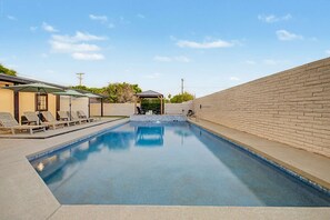 A rectangular swimming pool with a clear blue water surface, surrounded by a low brick wall and a covered seating area with lounge chairs. - NEW Ocotillo Luxe Retreat Scottsdale Old Town (Scottsdale)