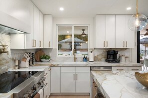 Una cocina moderna con armarios blancos, horno empotrado y cafetera.