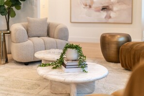 Ein modernes Wohnzimmer mit einem runden Couchtisch aus Marmor, einem grauen Sofa und einer Zierpflanze.