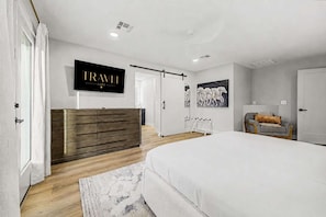 Ein modernes Schlafzimmer mit einem großen Bett, einer Holzkommode, einem an der Wand montierten Fernseher und einem Gemälde.